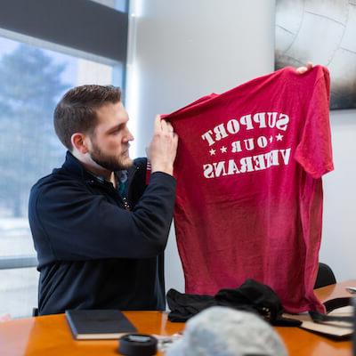 Man sitting at desk holds up tshirt that says 